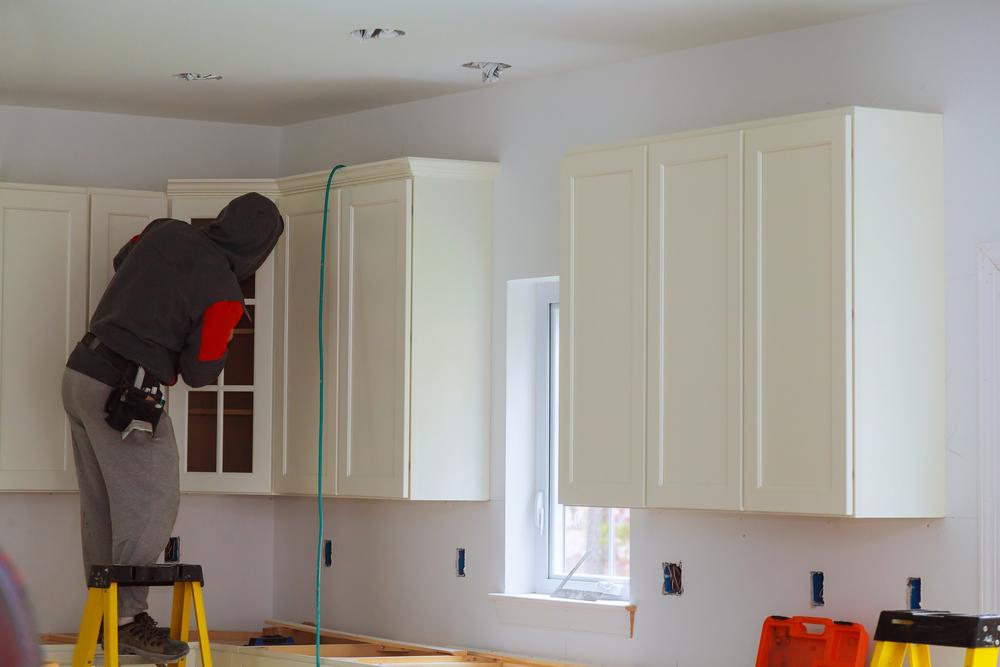 a man standing on a ladder installing Forevermark Cabinetry kitchen cabinets in a kitchen.