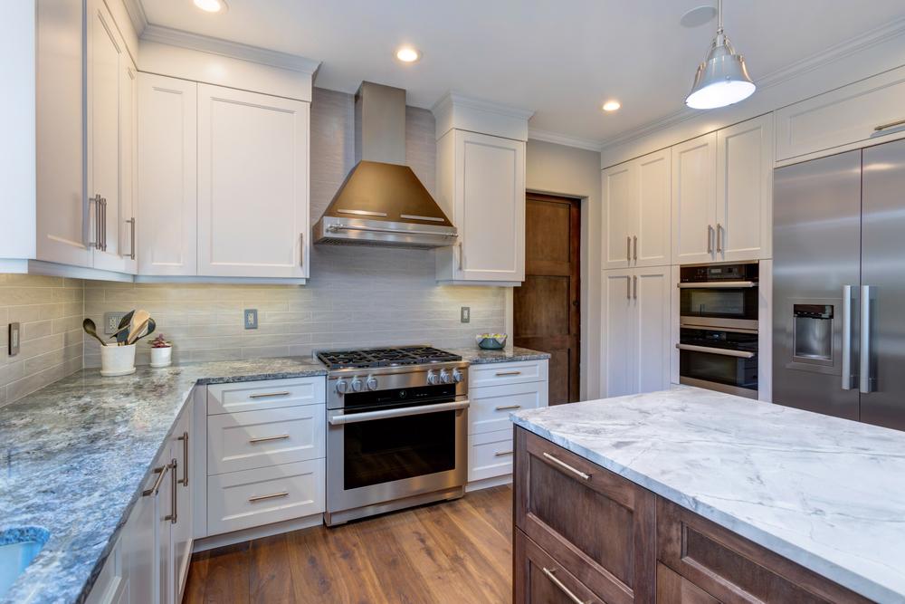 a white interior kitchen with marble island, exhaust hood and wooden cabinets from forevermark cabinetry